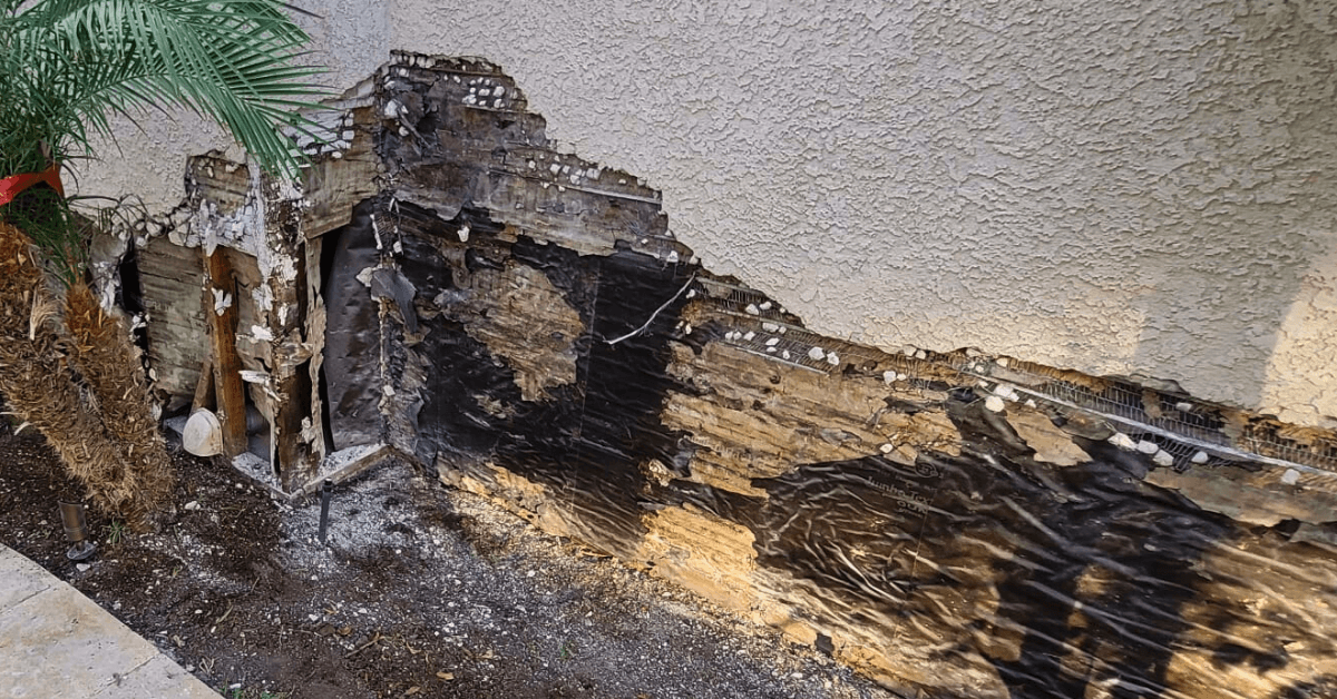 Destroyed building paper and severe damage exposed behind a stucco wall